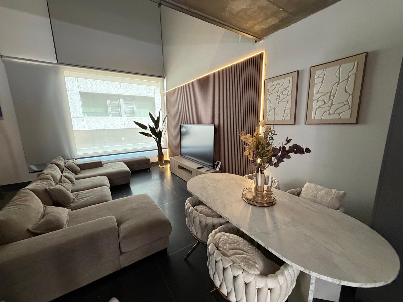 Salón reformado con panelado de madera, iluminación indirecta y comedor integrado